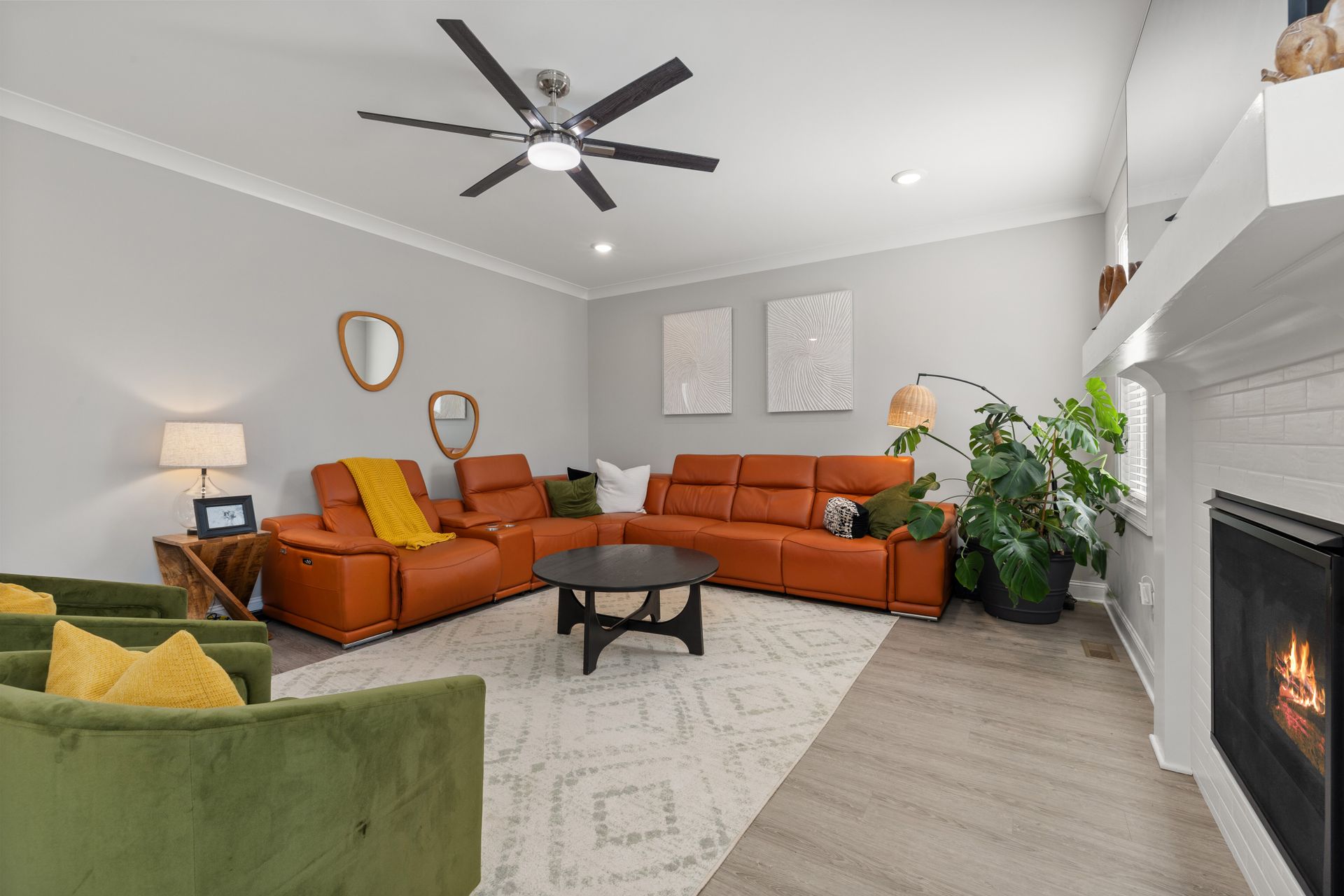 Bright residential living room with terracotta leather sofas, green velvet armchairs, yellow accents, indoor plants and a fireplace